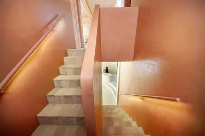 Looking down the stairwell, brick treads between warm clay walls with backlit handrails on both sides