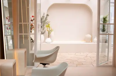 View through open glass doors to a stone-paved alcove, where an arched niche holds white vases and an olive branch