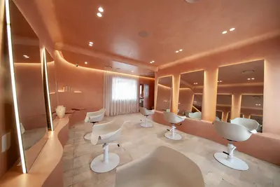 The main styling floor under a curved clay ceiling, with full-height backlit mirrors, white moulded chairs and a travertine floor