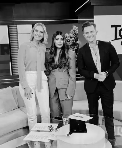 Black and white photograph of three people standing together on a television studio set beside a sofa and low round table