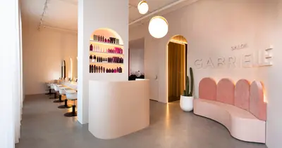 Wide view down the salon, from the arched product niche and globe pendants to the pink scalloped banquette under raised Salon Gabrielle lettering