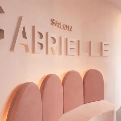 Raised Salon Gabrielle lettering on blush plaster above a row of arched pink velvet banquette backs