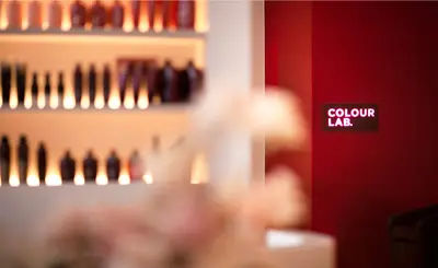 Backlit shelves of colour product in soft focus, with the deep red Colour Lab room beyond