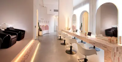 The styling floor, with arched mirrors above a veined stone counter and white moulded chairs on one side and black backwash chairs on the other