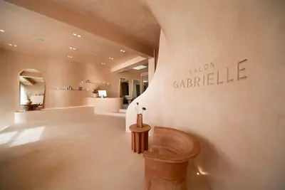 Curved clay-plaster entry with Salon Gabrielle incised into the wall, a terracotta pedestal stool and the reception counter beyond