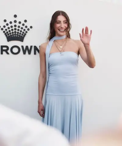 Guest waving in a pale blue halter dress in front of a Crown backdrop, hair in soft loose waves