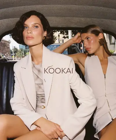 Two models in blush and cream tailoring seated in the back of a car on a city street