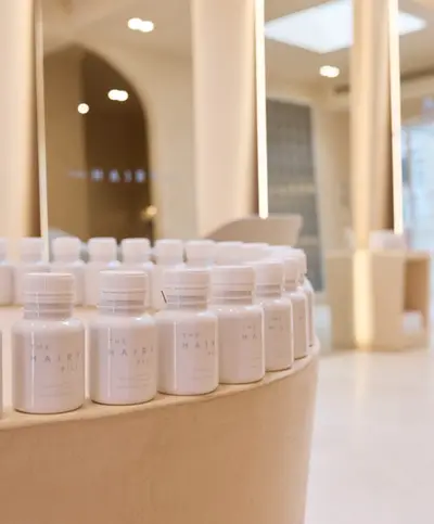 A row of white supplement bottles arranged along a curved plinth in the salon, with the mirrors and treatment chairs out of focus behind