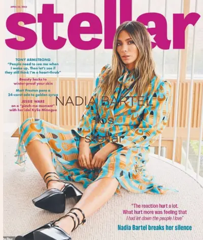 Magazine cover of a model in a patterned turquoise and orange dress seated against a white wall
