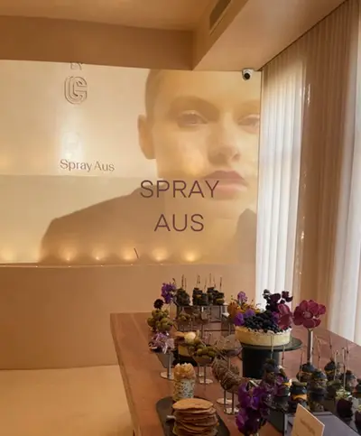 A brand film projected onto the salon wall above a table of desserts and flowers, lit warmly from below
