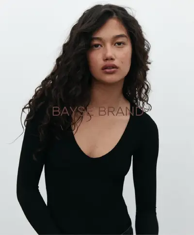 Model in a black scoop-neck top against a white backdrop, hair falling in long dark curls