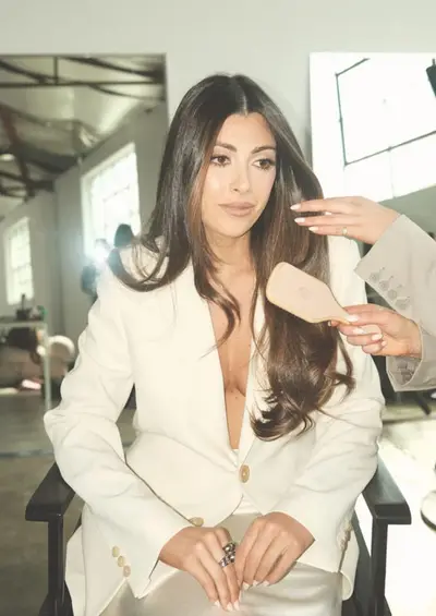 A client in a cream blazer having her long brunette hair brushed out beside the salon window