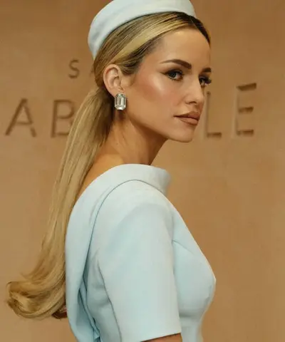 Guest in profile in a pale blue pillbox hat and dress, hair in a long straight ponytail, against raised Salon Gabrielle lettering