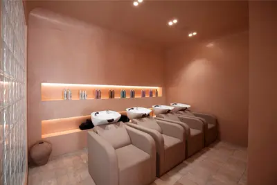 The backwash room, with four basins and beige chairs against terracotta plaster below a long backlit niche of product bottles