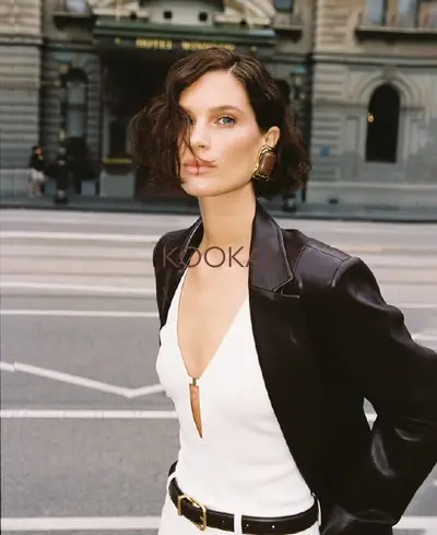Model on a city street in a dark leather jacket over a white plunge-front top, hair short and tousled