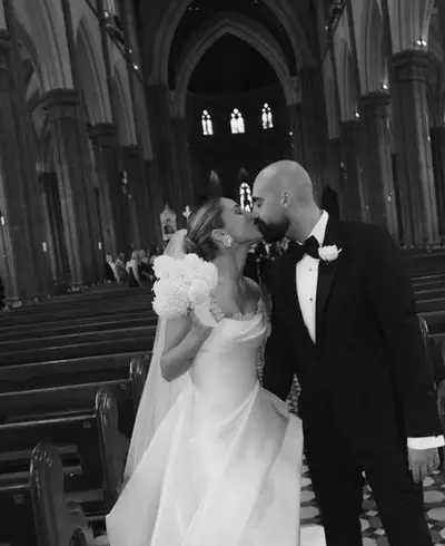 Black-and-white photograph of a bride and groom kissing in a cathedral aisle, her hair in a sculpted low bun