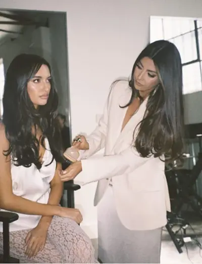 Gabrielle spraying a seated client's hair, both in cream and blush